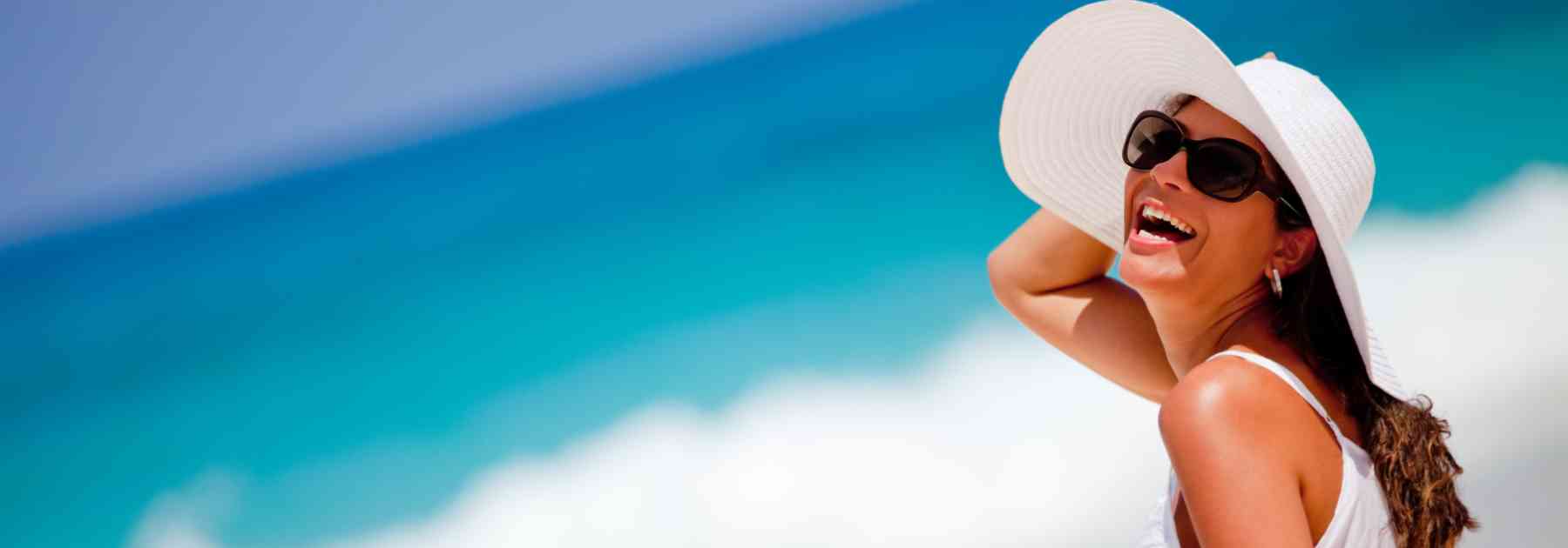 woman in sun hat and sunglasses smiling on beach