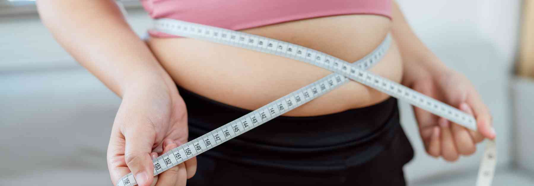 overweight woman in pink shirt measuring waist