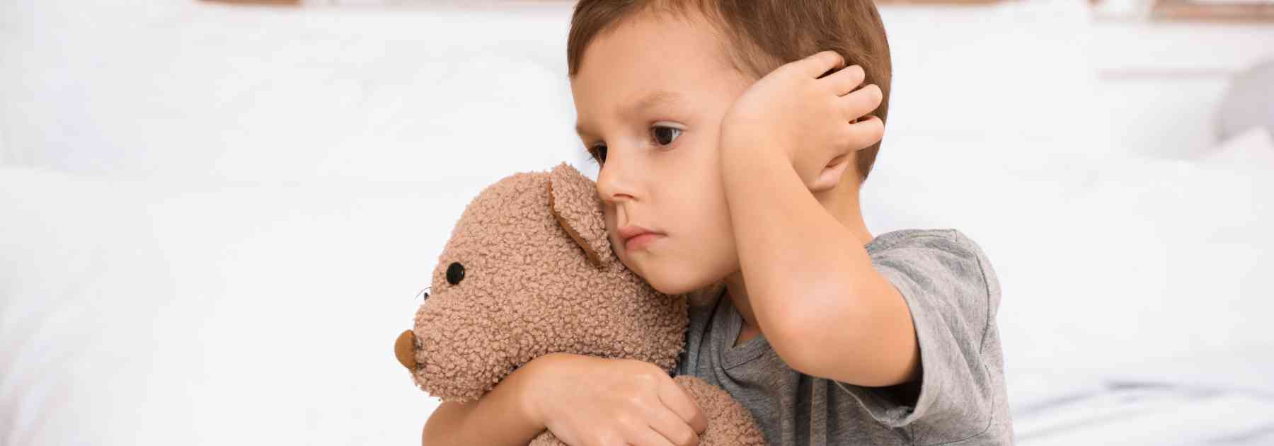 child clutching teddy bear and holding ear