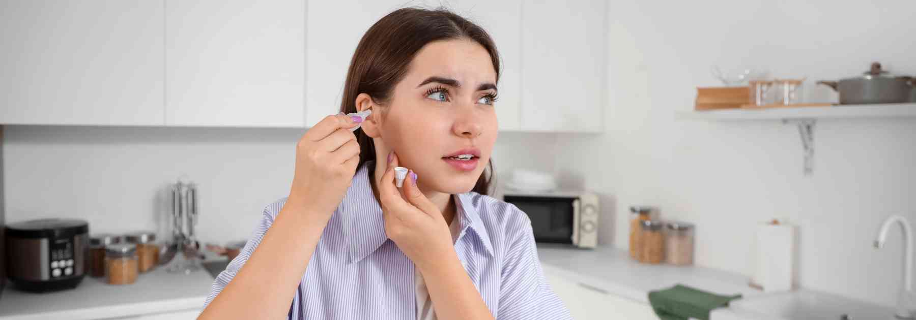 young woman putting ear drops in her ear in kitchen