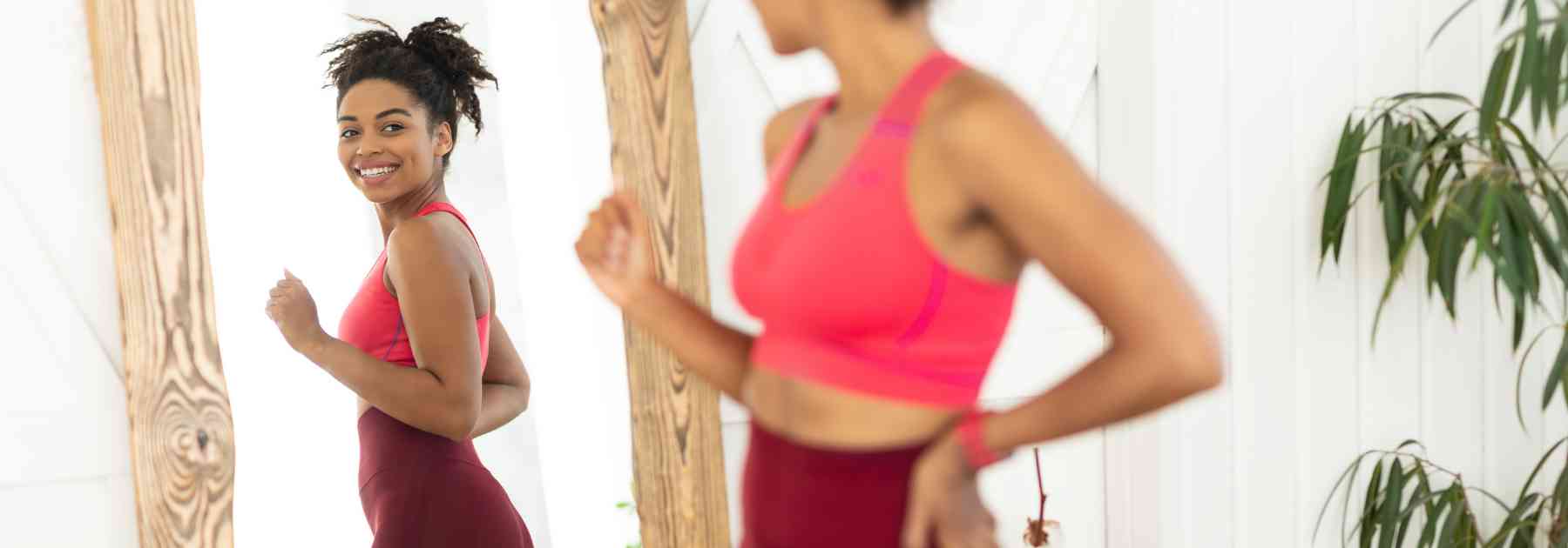 woman in workout gear smiling and looking in mirror