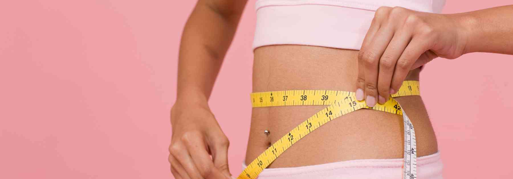 woman measuring waist on pink background