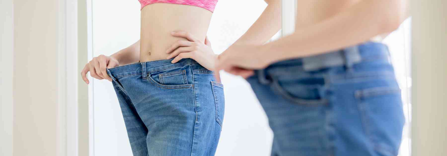 woman in jeans too big looking in mirror