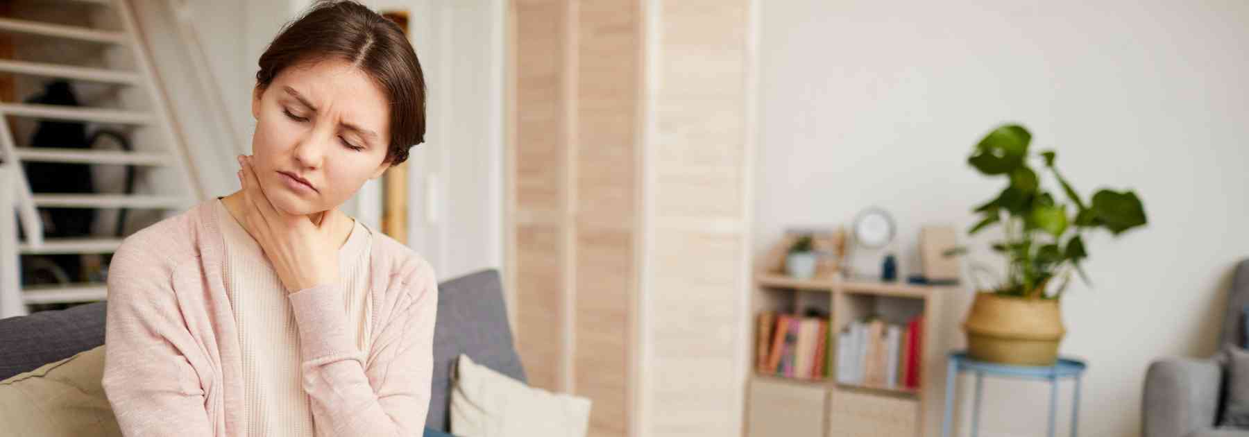woman sitting on couch clutching her throat in discomfort