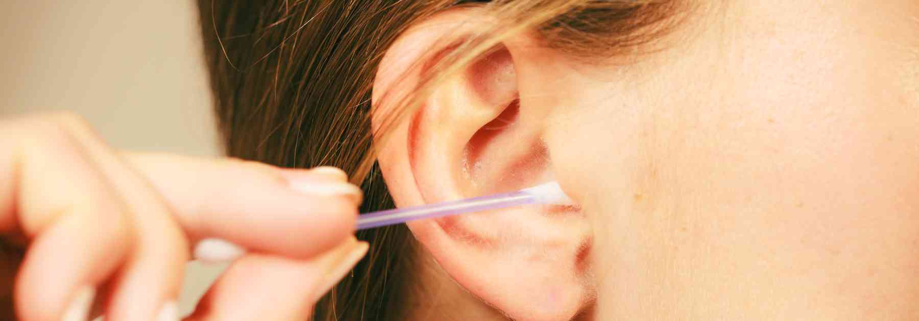young woman inserting cotton bud into her ear