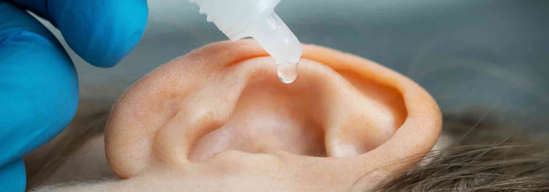 person wearing medical glove inserting ear drops into their ear