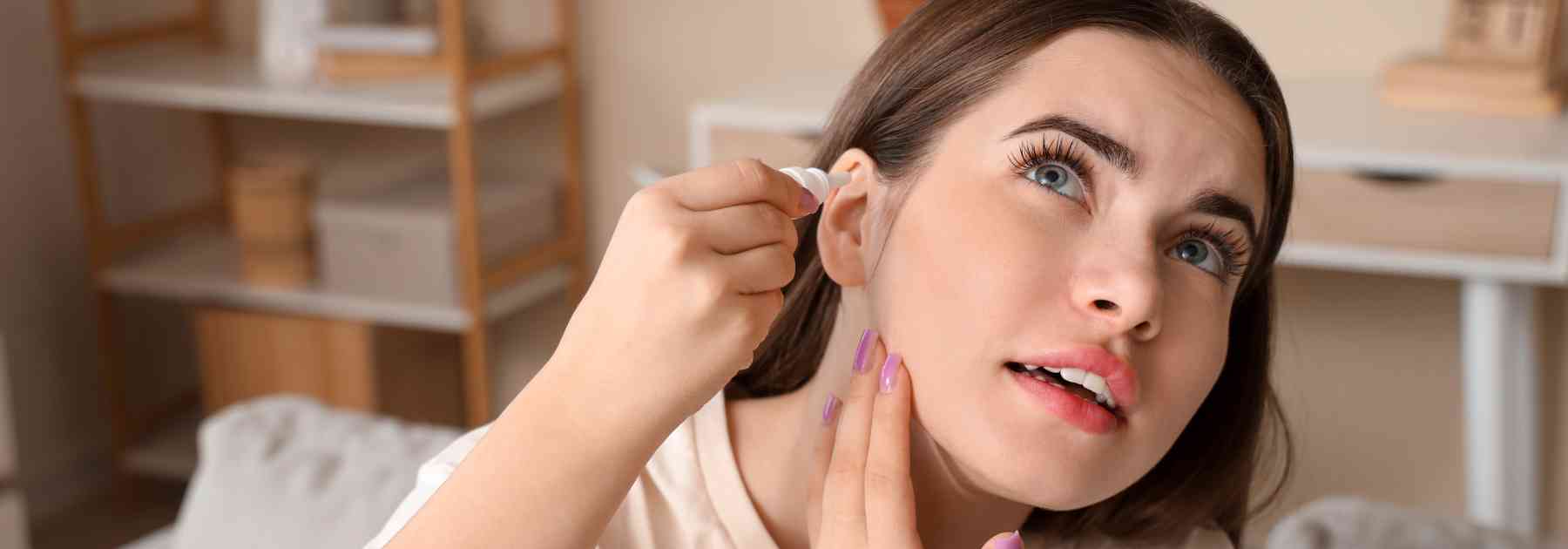 young woman inserting ear drops into her ear