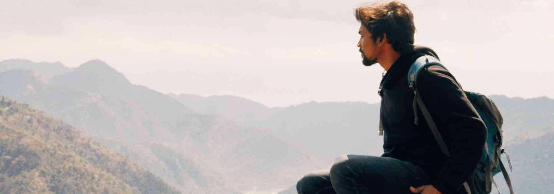male traveller wearing backpack admiring view of mountains