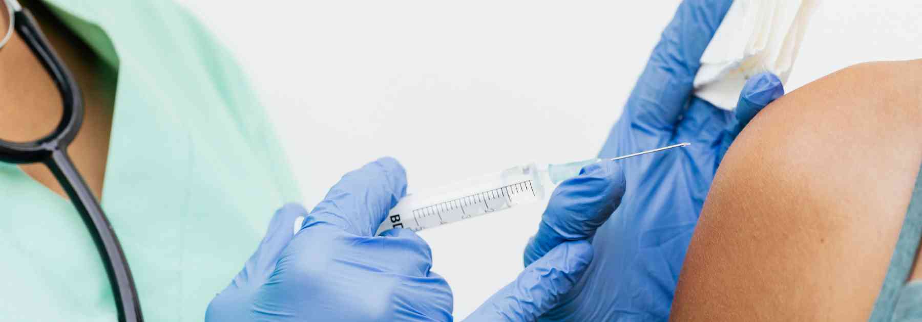 patient in green shirt receiving vaccine from medical professional