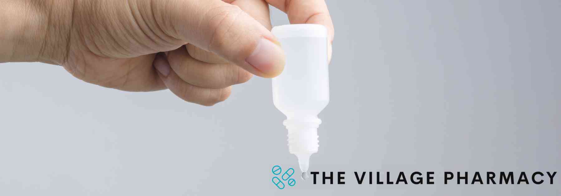 person holding bottle of ear drops upside down on grey background